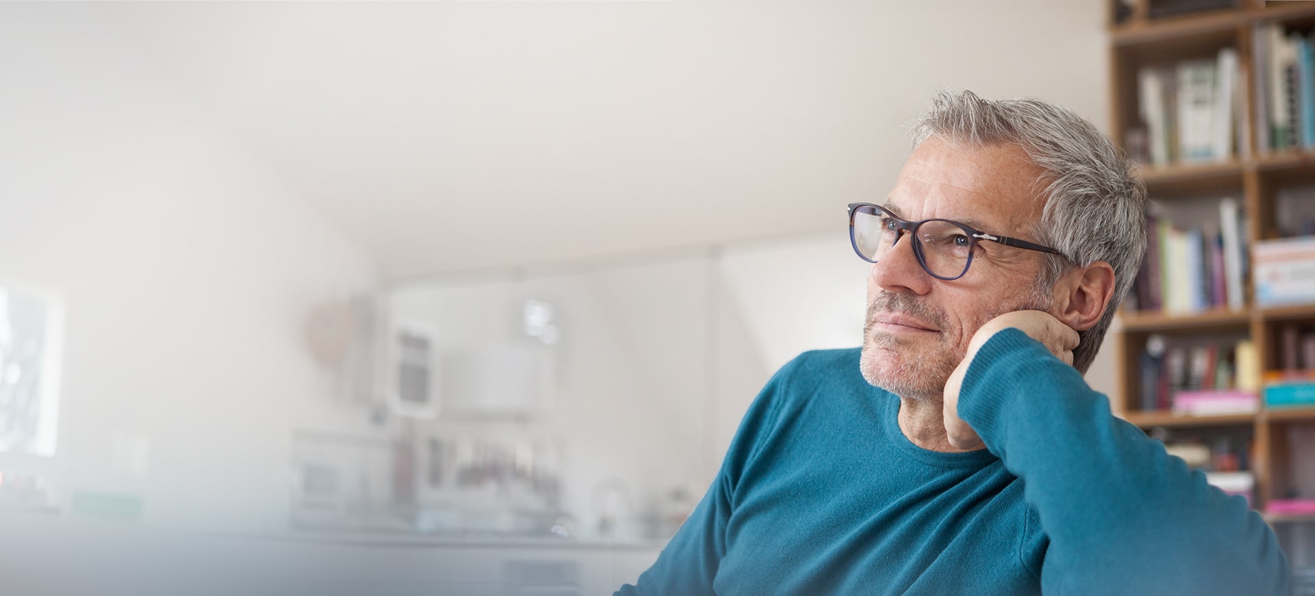 Mann mit Brille sitzt lächelnd in seiner Wohnung.