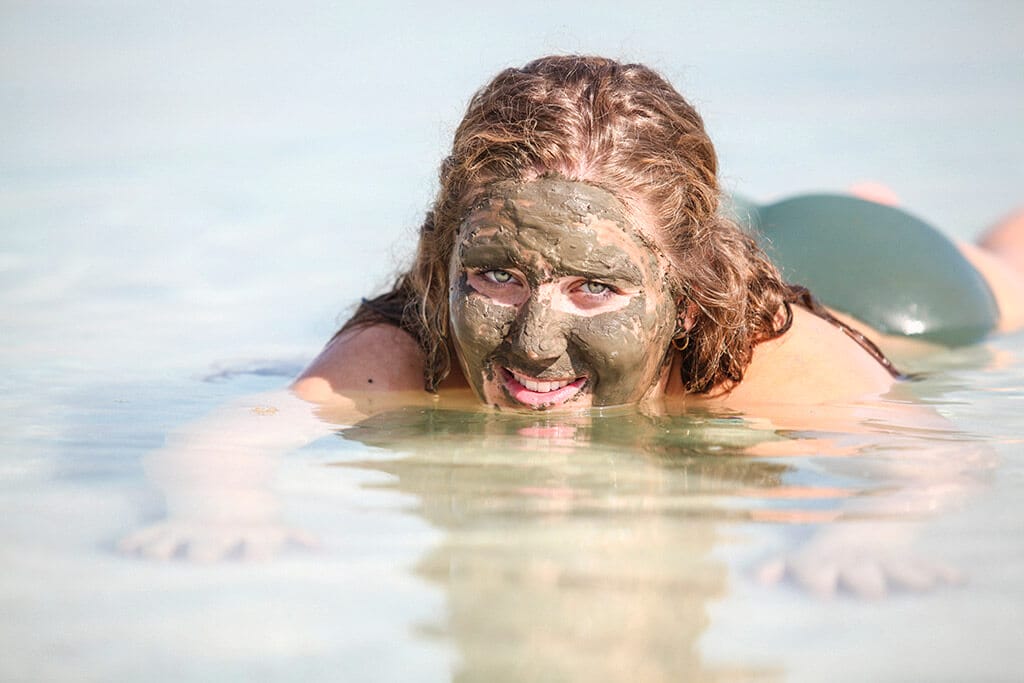 Eine junge Frau in einem grünen Bikini liegt im Wasser und hat eine grüne Maske im Gesicht.