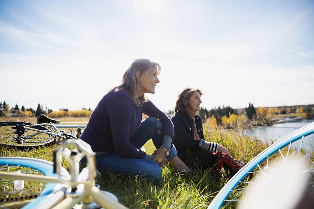 Zwei ältere Frauen ruhen sich an einem See von ihrer Fahrradtour aus.