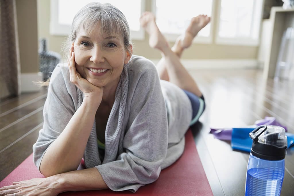 Eine Frau liegt auf einer Yogamatte und lächelt in die Kamera.