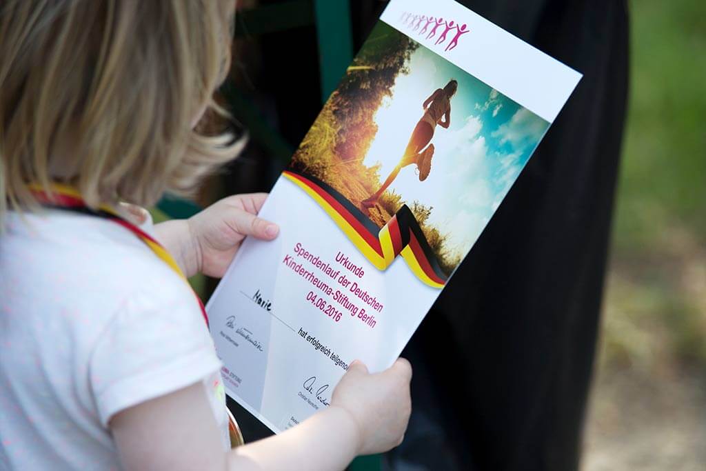 Ein Kind hält eine Urkunde vom Spendenlauf der Kinderrheuma-Stiftung in der Hand.