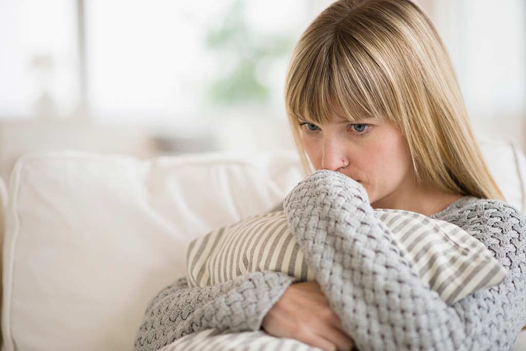 Frau sitzt auf einem Sofa und drückt ein Kissen an sich.