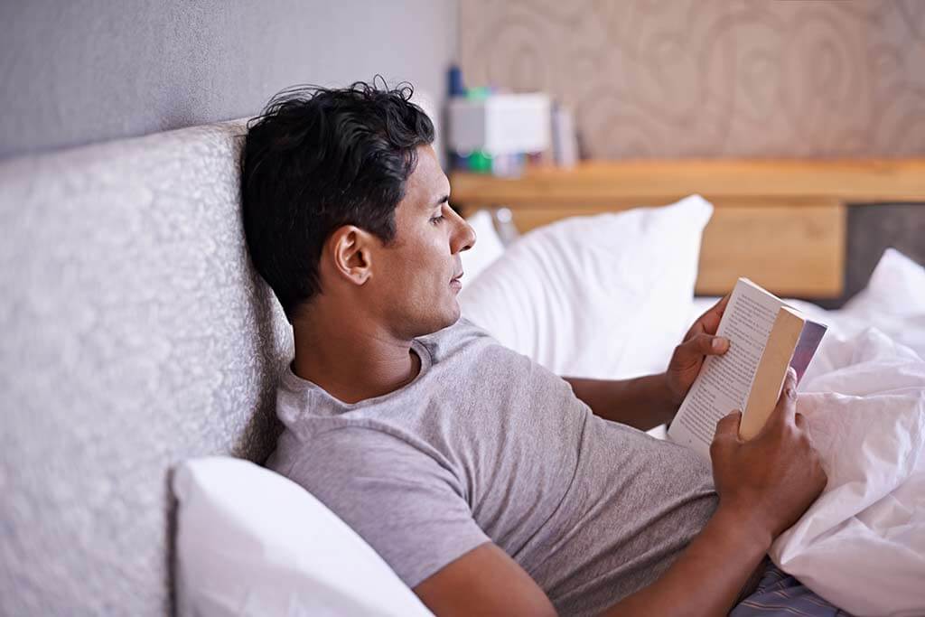 Mann liegt im Bett und liest ein Buch.