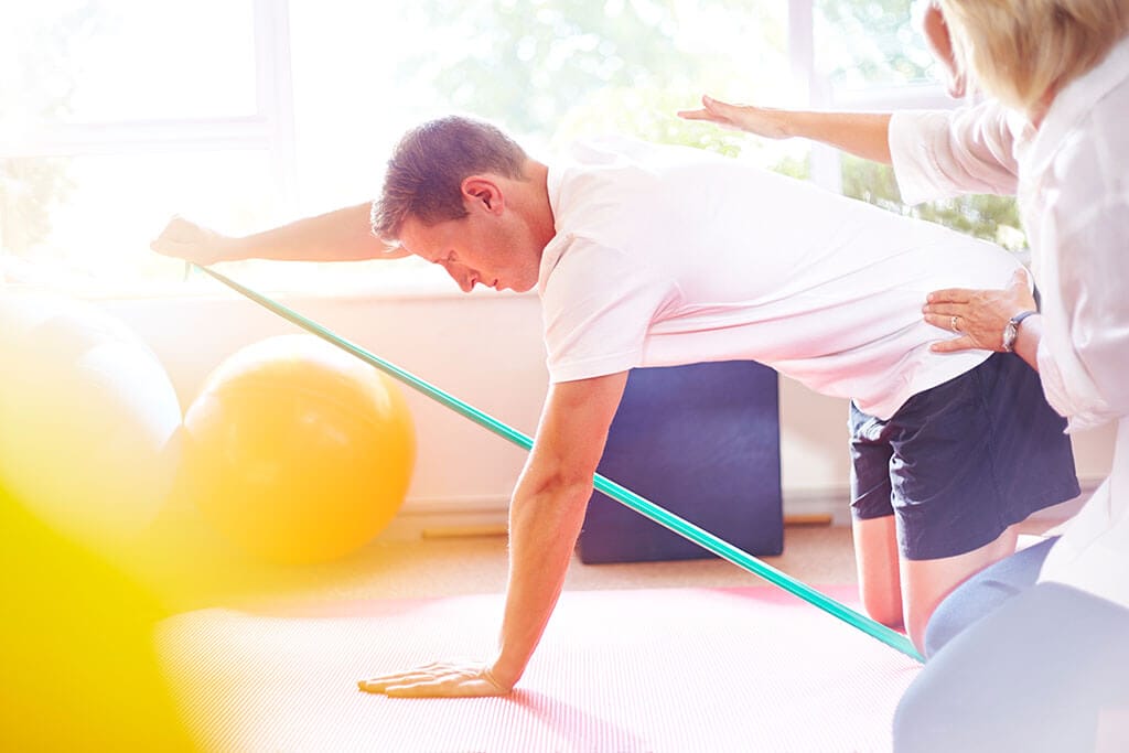 Ein Mann macht mti einem Gummiband Gymnastikübungen auf dem Boden.