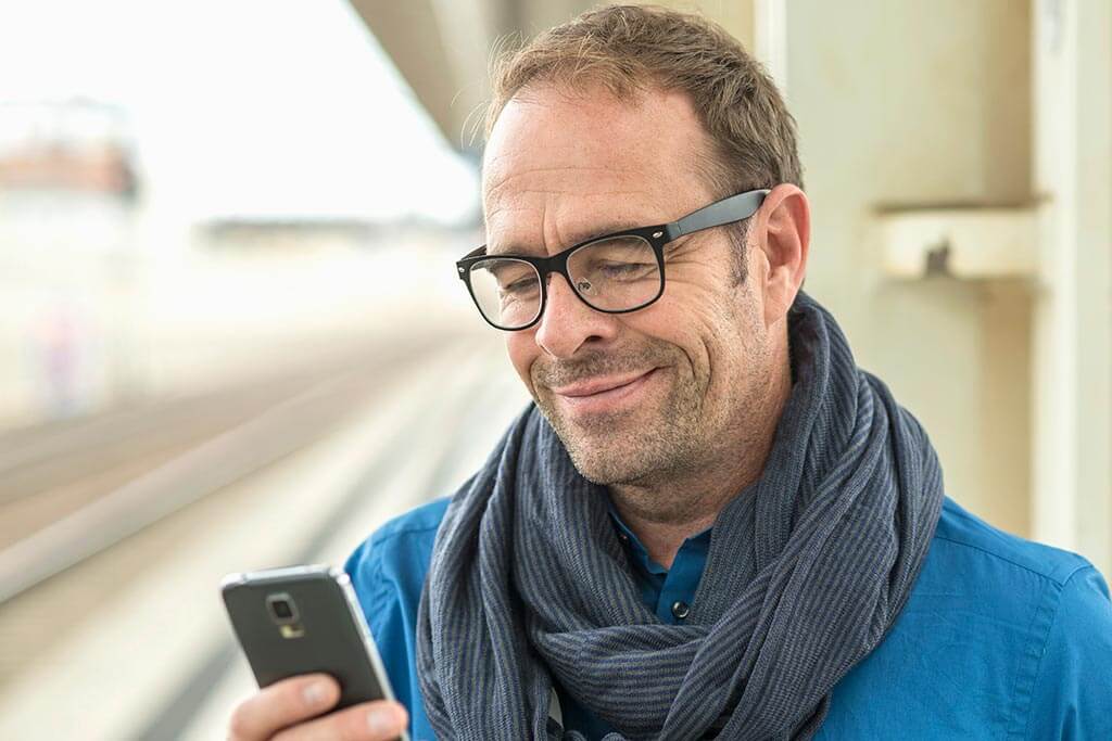 Ein Mann schaut lächelnd auf sein Handy.