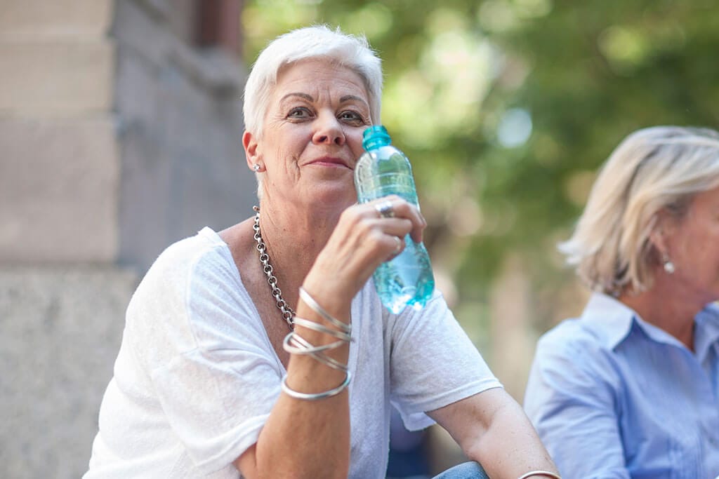 Eine Frau trinkt aus einer blauen Flasche.