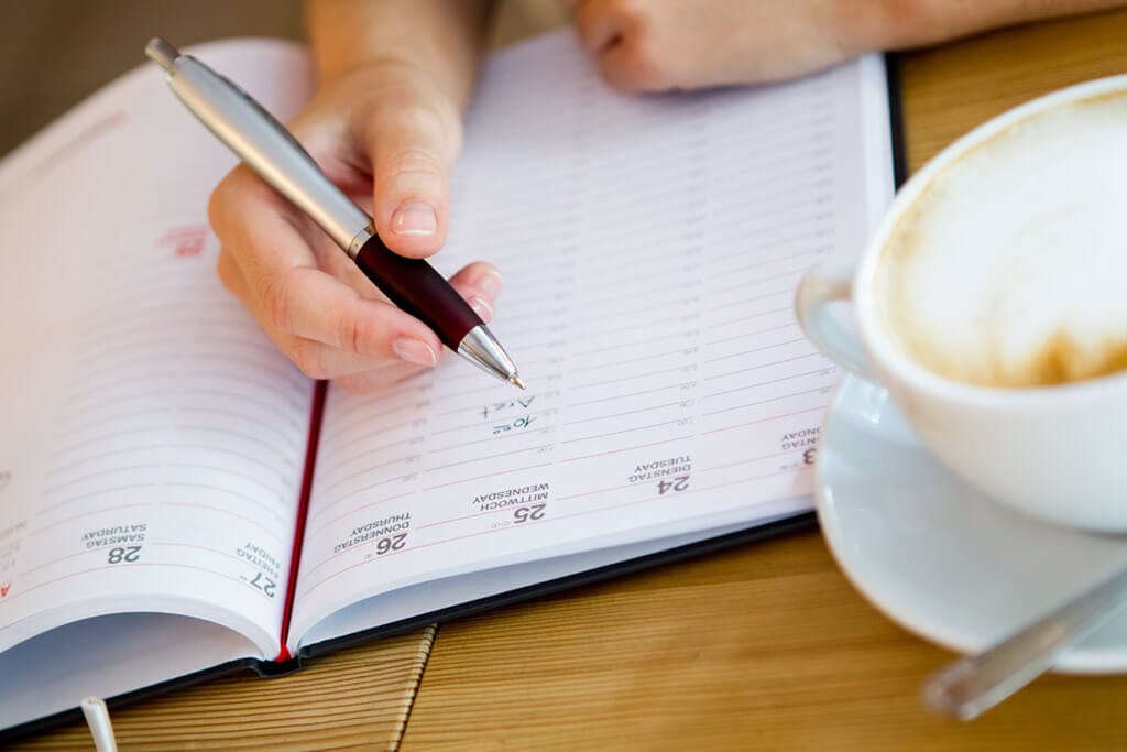 Eine Person hält einen Stift und schreibt etwas in einen Buchkalender