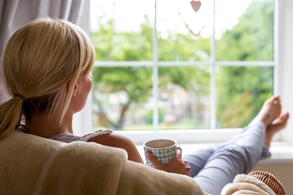 Frau mit Tasse in der Hand schaut aus dem Fenster