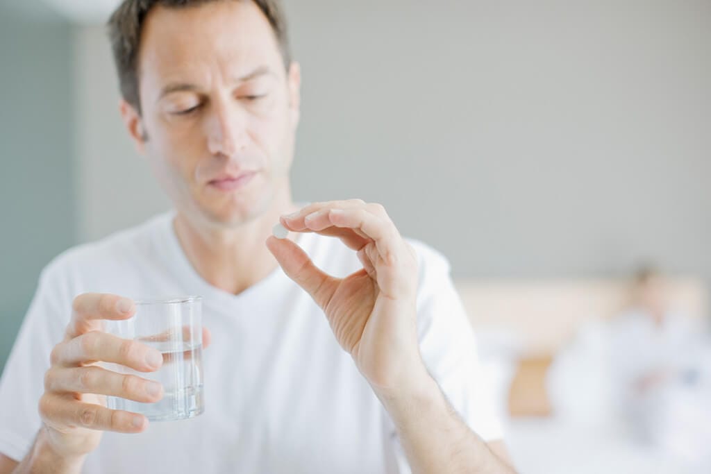 Mann hält ein Glas und eine Tablette in der Hand