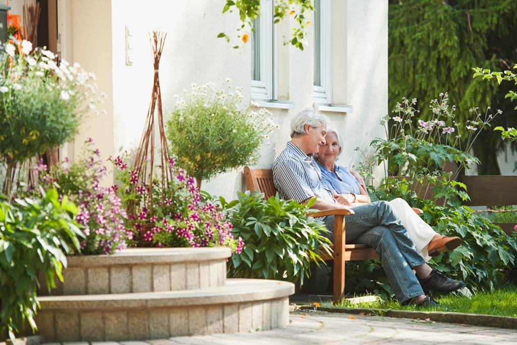 Altes Ehepaar sitzt auf einer Bank im Garten