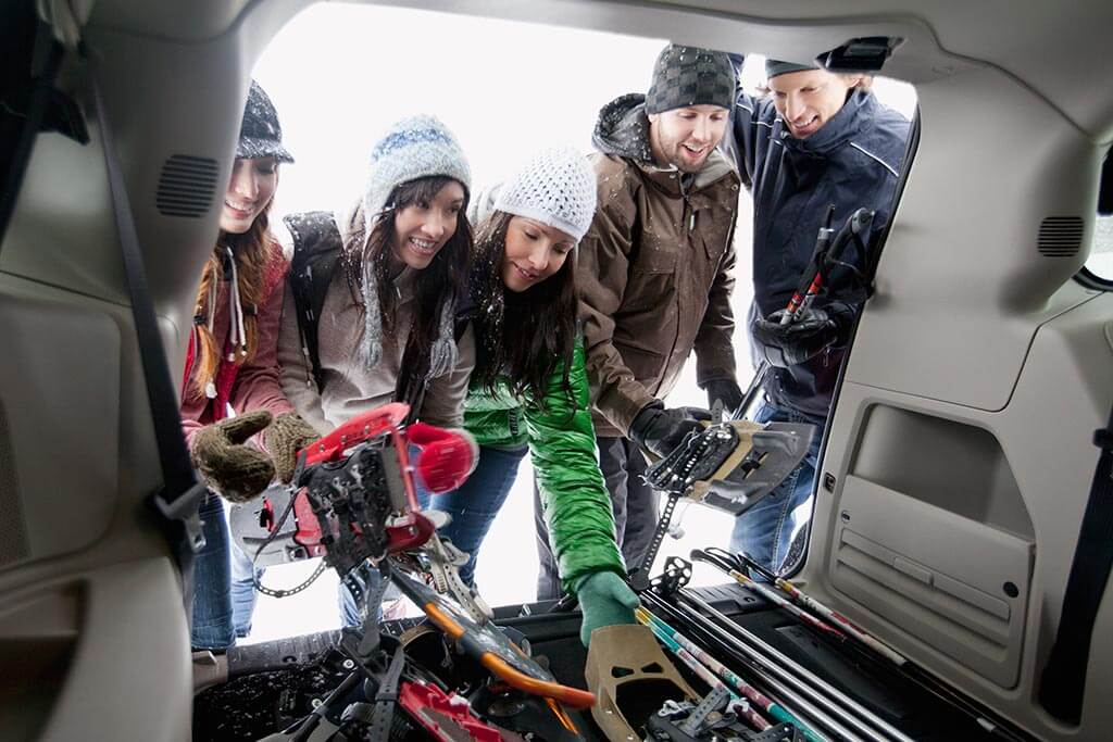 Eine Gruppe von jungen Menschen räumen ihre Skisachen in das Auto hinein.