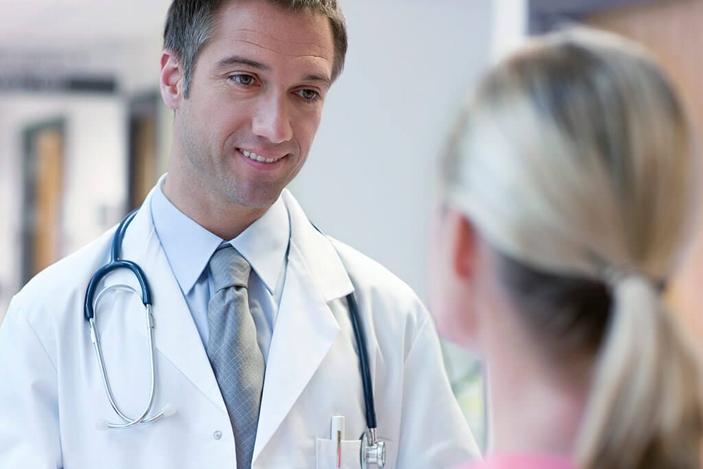 Junger Arzt lächelt seine Patientin an.