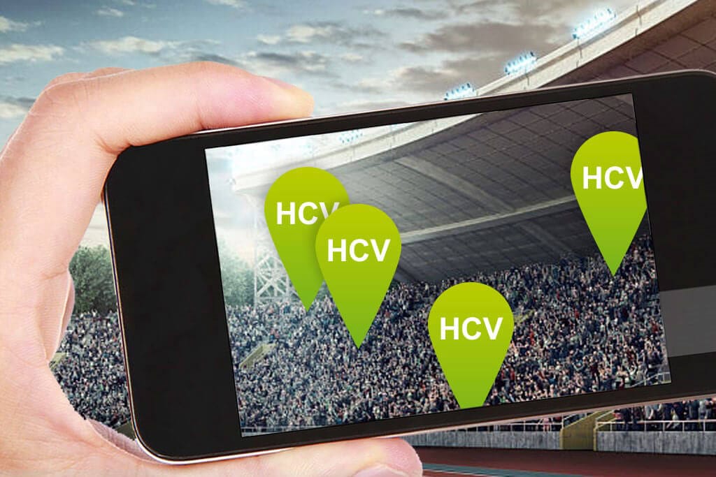 Eine Hand mit einem Smartphone fotografiert die Menschenmenge in einem Stadion.