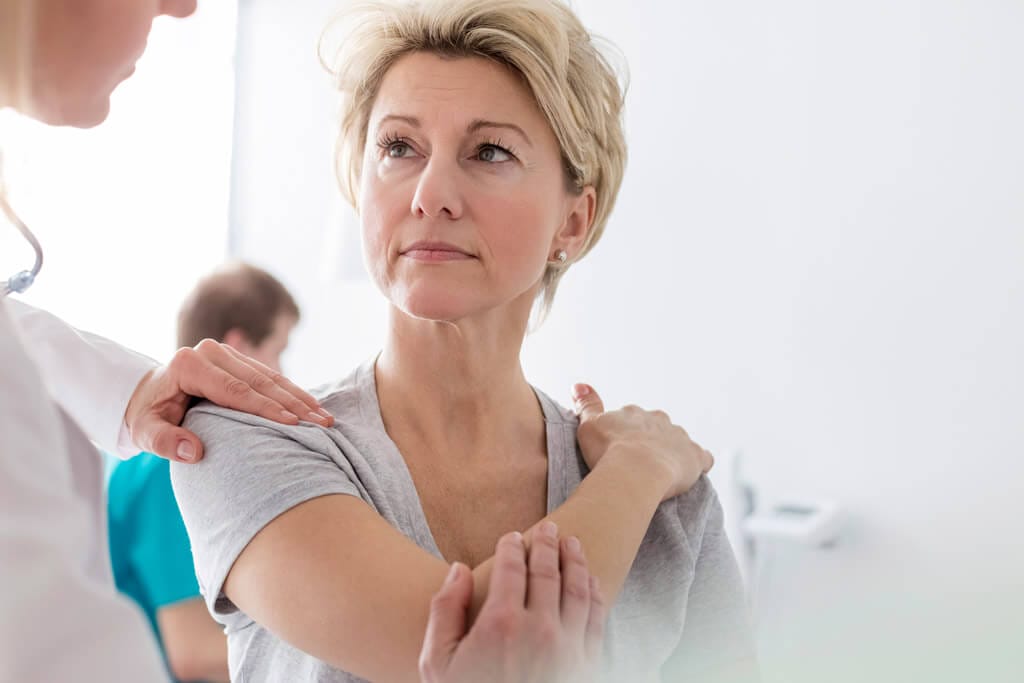 Frau hält sich den Arm und wird vom Arzt behandelt