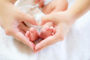 Zwei Hände formen ein Herz über Babyfüße