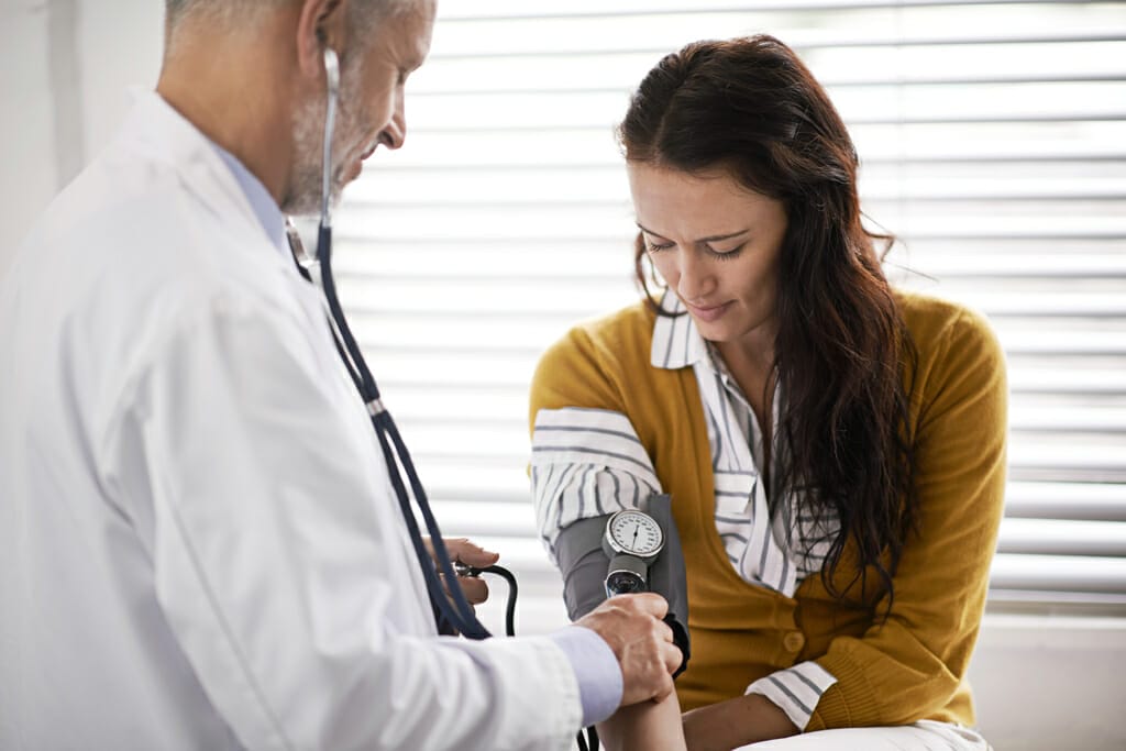 Einer jungen Frau wird der Blutdruck von Ihrem Arzt gemessen