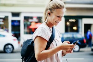 Eine Frau mit einem Rucksack auf dem Rücken schaut auf Ihr Smartphone.