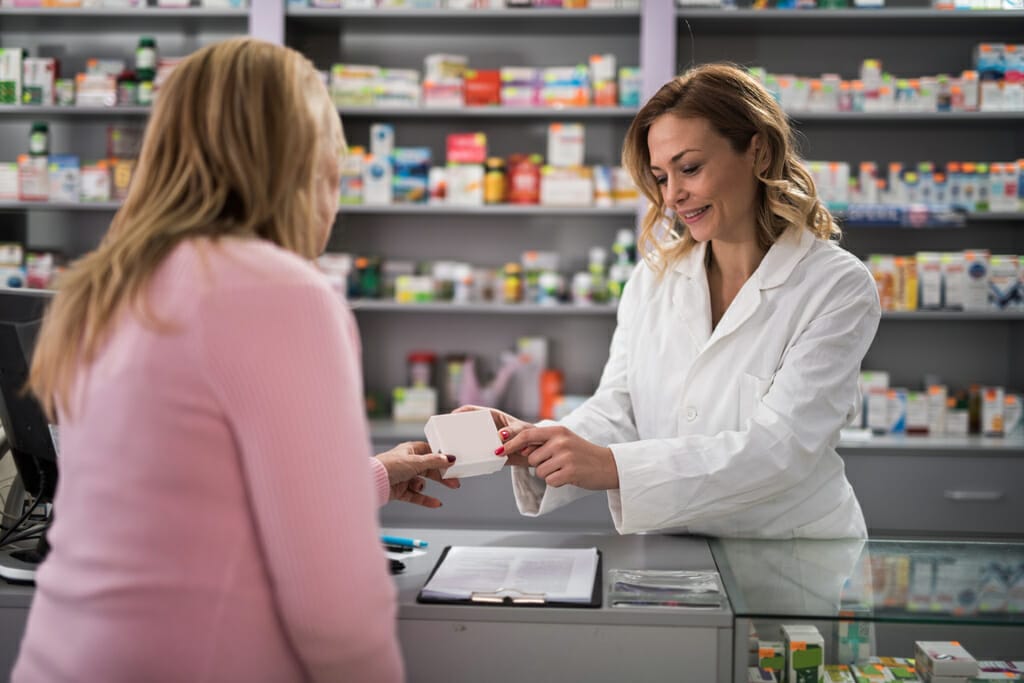 Eine Apothekerin überreicht der Kundin ein Medikament.