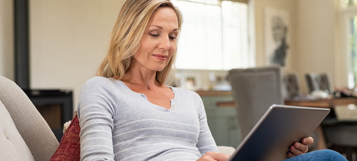 Frau sitzt auf der Couch und füllt einen Test auf dem Tablet aus