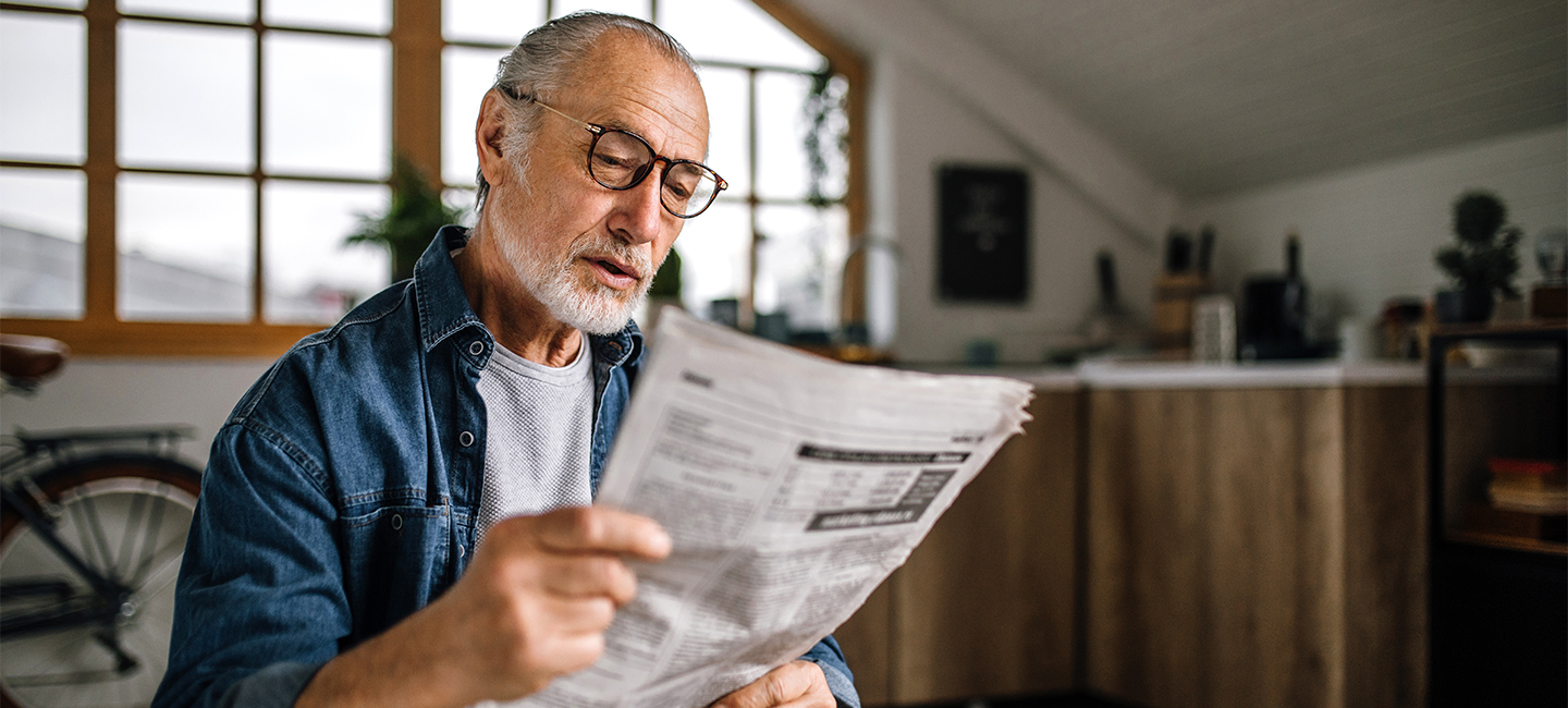 Älterer Mann am Esstisch mit Zeitung in der Hand
