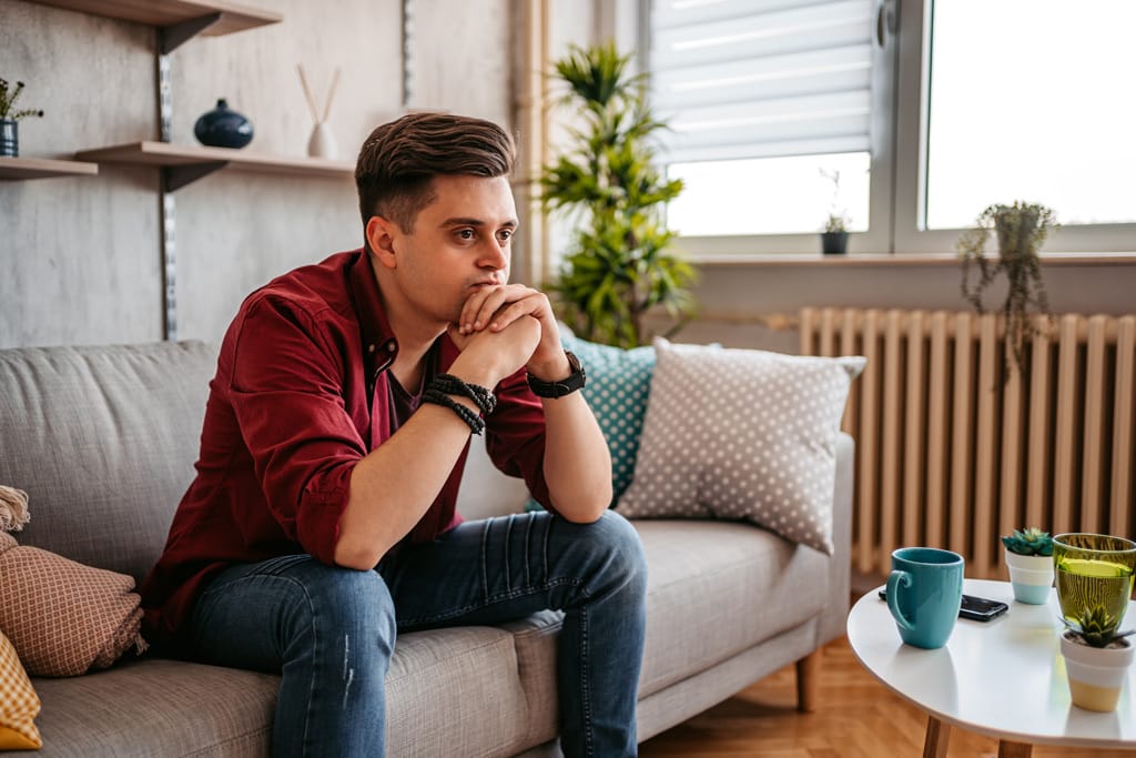 Junger Mann sitt auf dem Sofa und denkt nach