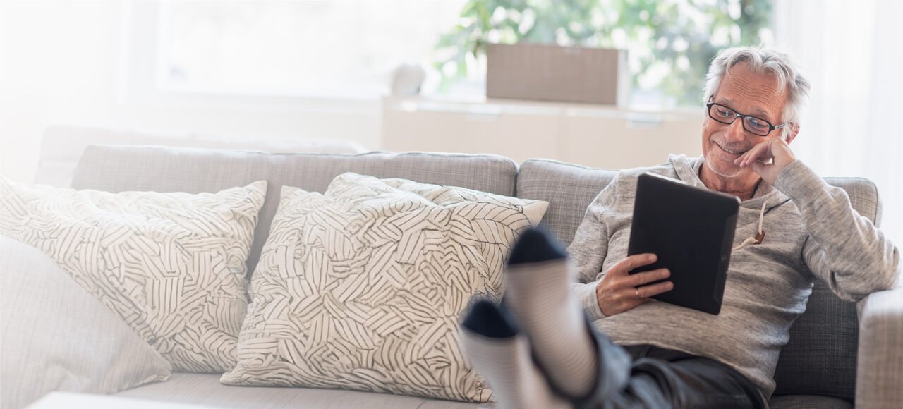 Ein Mann sitzt auf dem Sofa und informiert sich am Tablet über die überaktive Blase