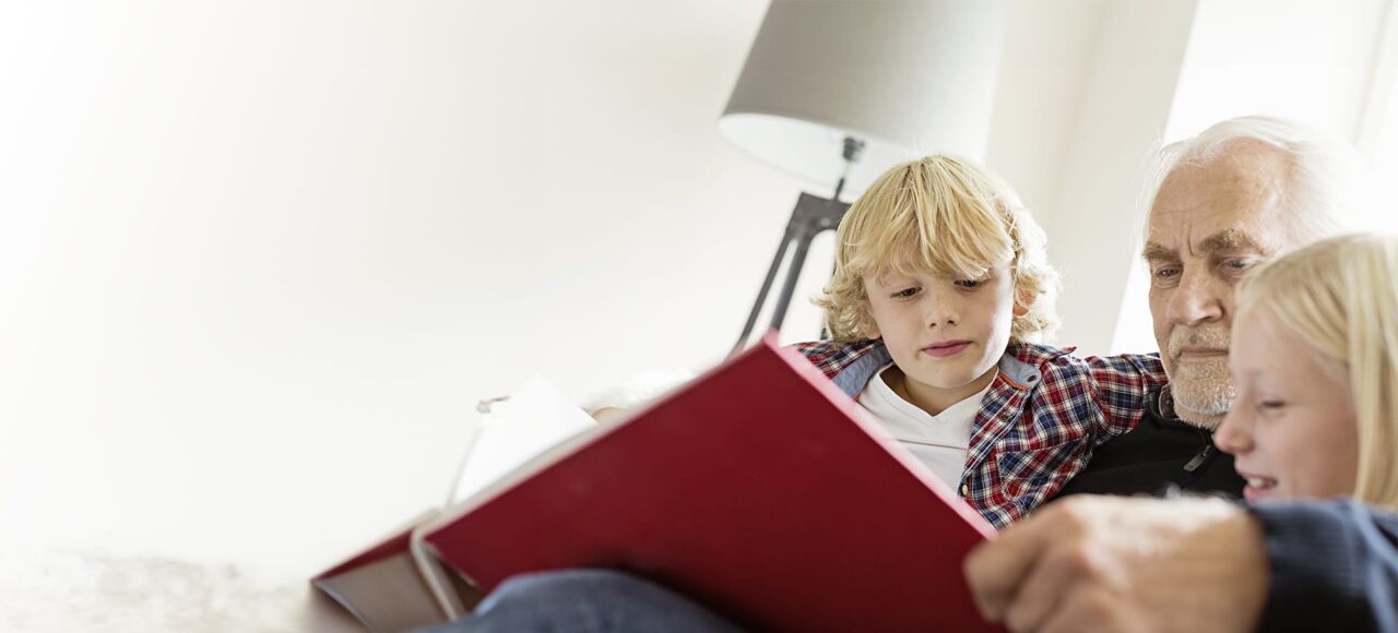 Ein älterer Mann schaut ein Buch mit seinen Enkelkindern an.