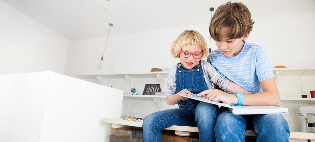 Bruder und Schwester sitzen auf der Küchzeile und schauen ein Backbuch an