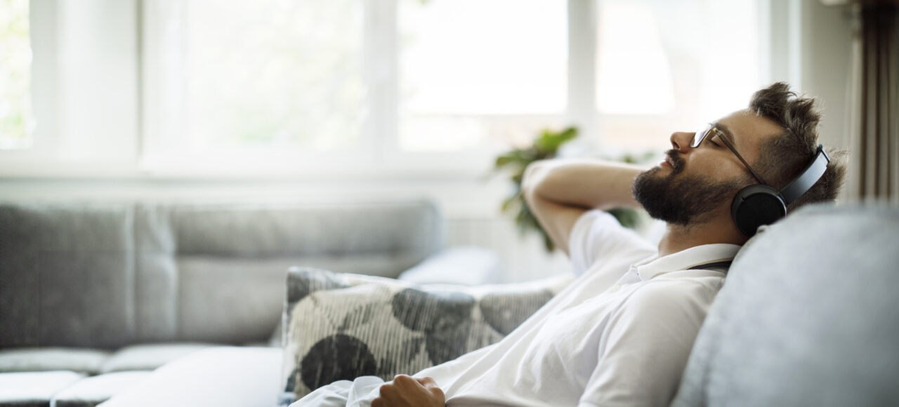 Junger Mann sitzt auf dem Sofa und hört Musik mit Kopfhörern