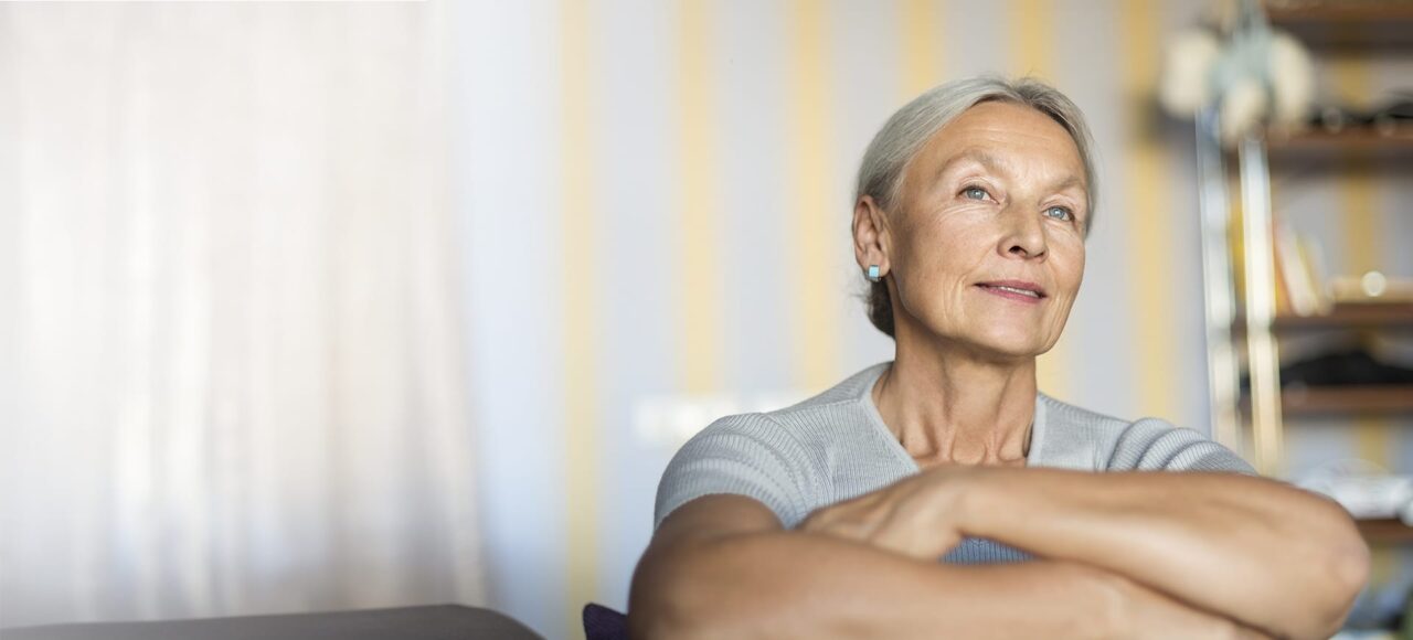 Reife Frau sitzt auf dem Sofa und schaut in die Ferne