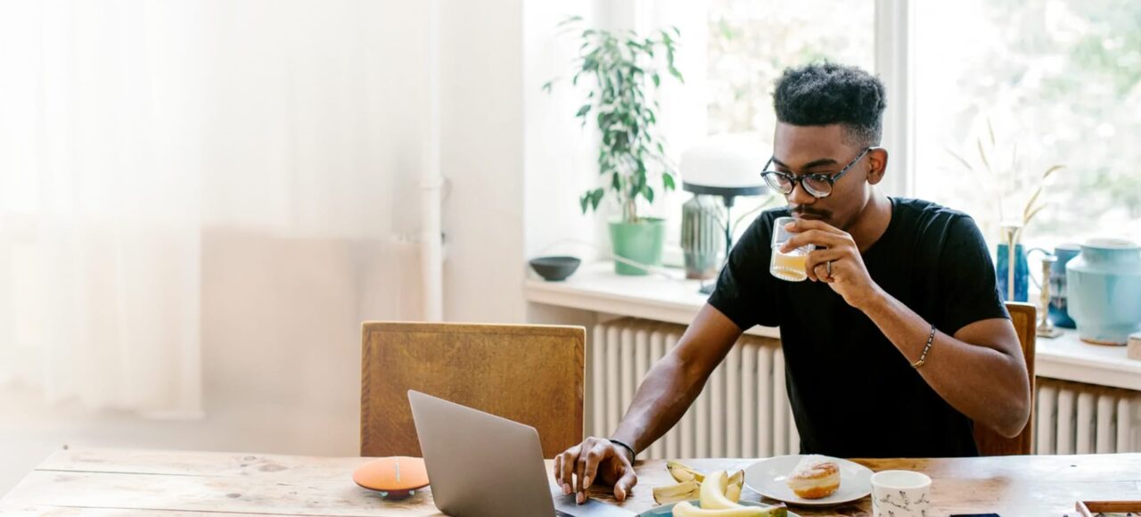 Junger Mann sitzt beim Frühstück und schaut etwas im Laptop nach