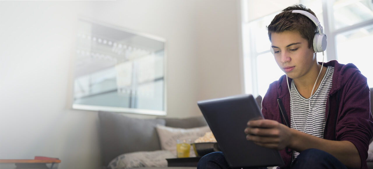 Ein Teenager hat Kopfhörer auf schaut etwas auf dem Tablet an