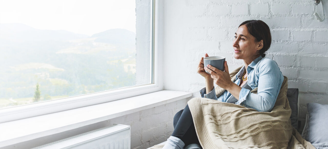 Eine Frau mit Uveitis trinkt einen Tee auf dem Sofa und schaut aus dem Fenster