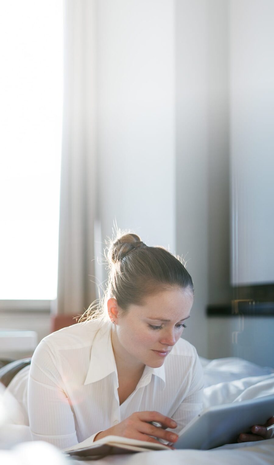 Eine junge Frau liegt im Bett und schaut auf ihr Tablet.