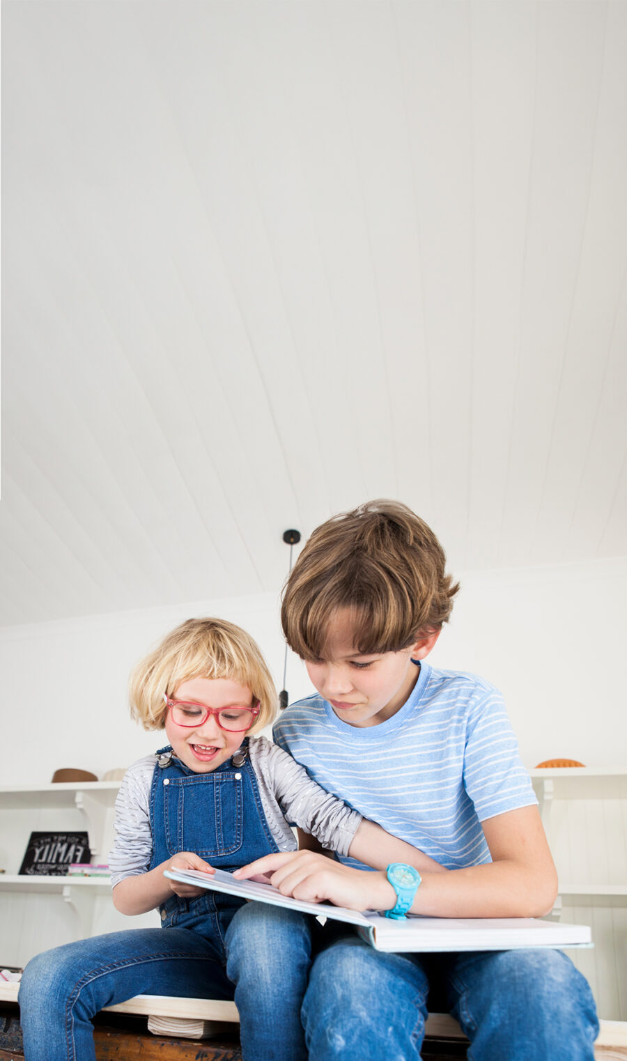 Bruder und Schwester sitzen auf der Küchzeile und schauen ein Backbuch an