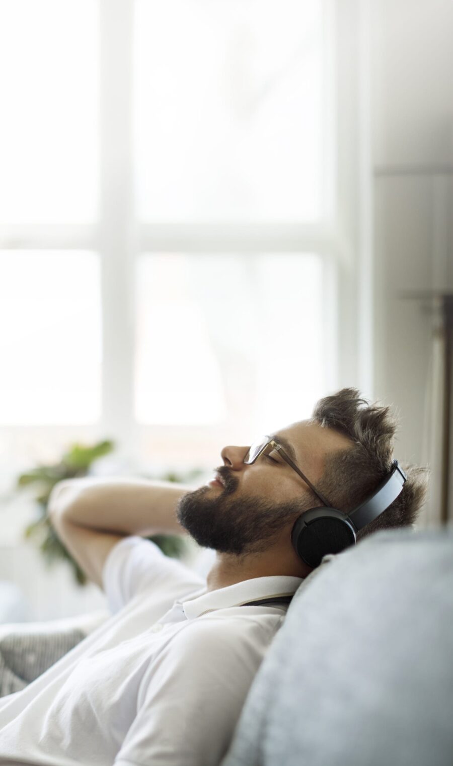 Junger Mann sitzt auf dem Sofa und hört Musik mit Kopfhörern