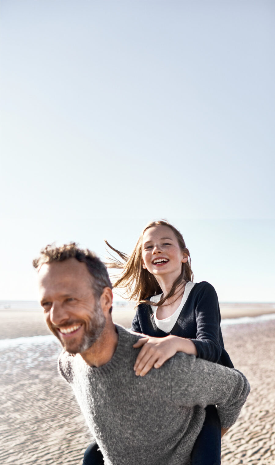 Ein Vater trägt seine Tochter auf dem Rücken über den Strand