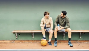 Vater und Sohn machen eine Pause vom Sport und sitzen auf der Bank um etwas zu trinken