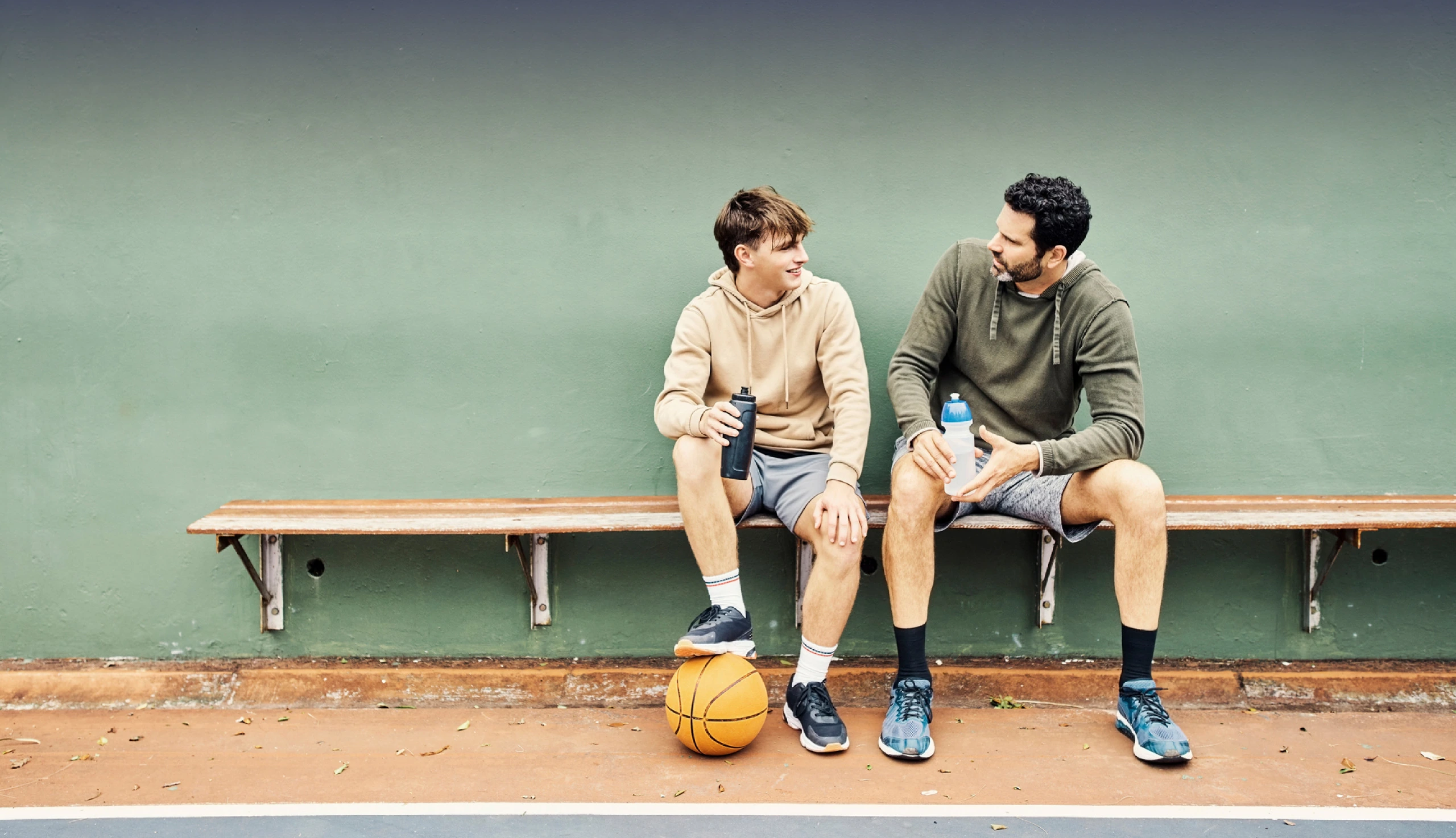 Vater und Sohn machen eine Pause vom Sport und sitzen auf der Bank um etwas zu trinken