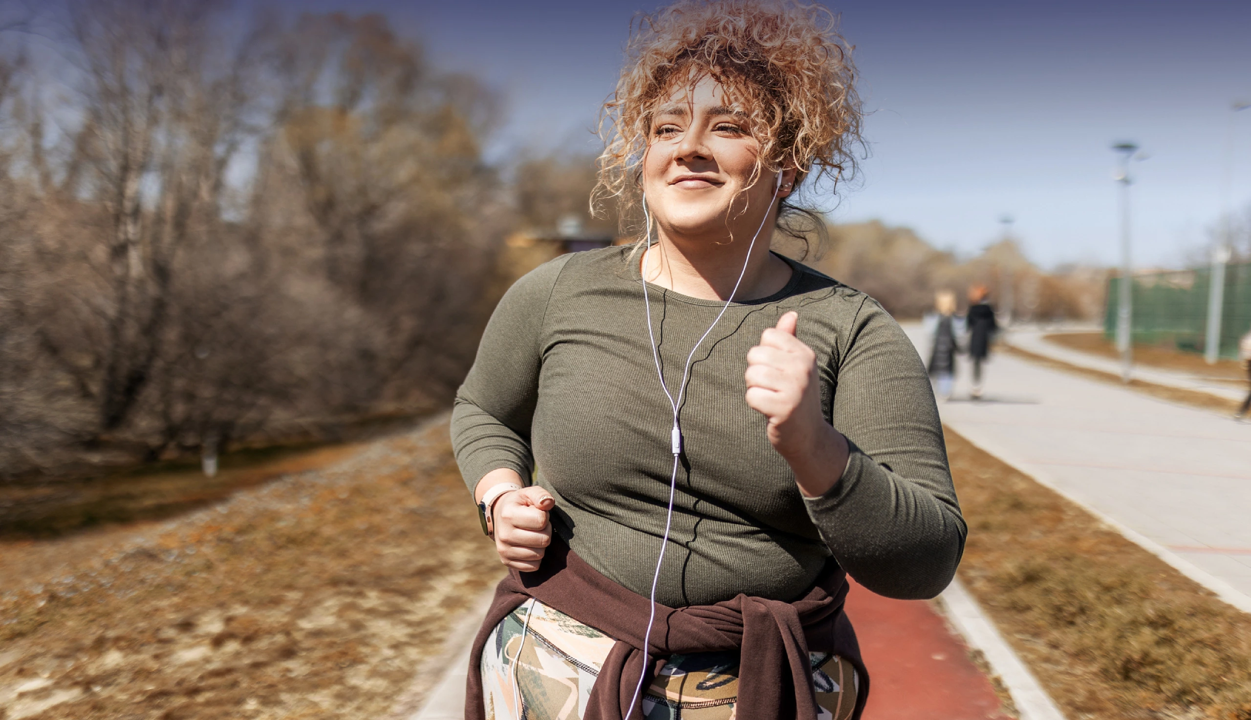 Frau mit blonden Locken joggt draußen und hat ihre Jacke um die Hüfte gebunden.