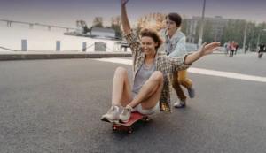 Eine Mutter mit kuzren Haaren lässt sich von ihrem Sohn auf dem Skateboard anschieben.
