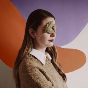 Frau mit Blatt vor Gesicht vor hellem Hintergrund