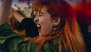 Junge Frau mit langen roten Haaren und Glitzer im Gesicht freut sich sehr