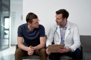 Arzt und Mann mit Migräne im Gespräch im Wartezimmer.