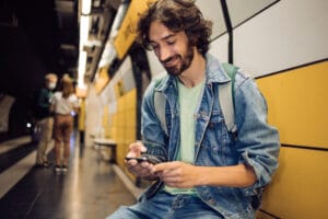 Mann in U-Bahn Station mit Handy und Jeansjacke