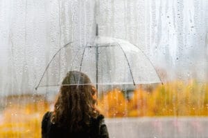 Frau mit langen braunen Haaren, von hinten abgebildet, steht unter Regenschirm