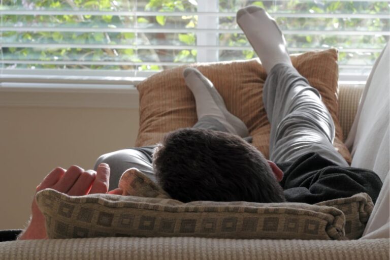 Mann mit Migräne liegt auf der Couch, von hinten zu sehen