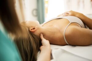 Frau mit Migräne auf dem Massagetisch, Hand im Nacken