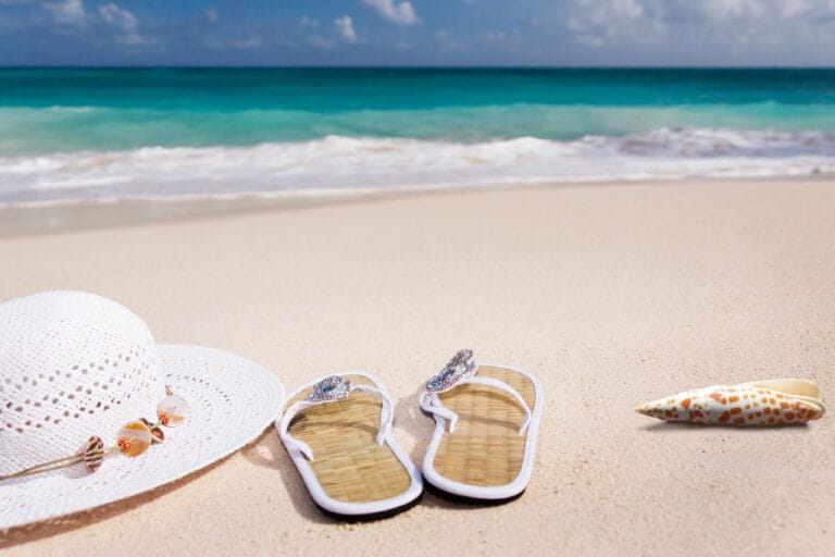Ein Sonnenhut, ein paar Sandalen und eine Muschel am Strand