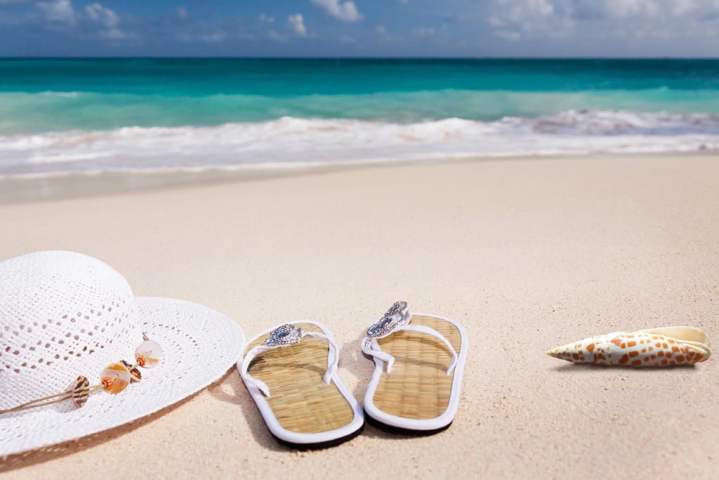 Ein Sonnenhut, ein paar Sandalen und eine Muschel am Strand
